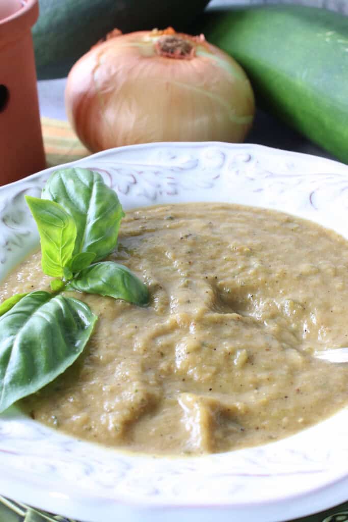 A creamy Roasted garlic and zucchini soup in a bowl with a sprig of fresh basil.