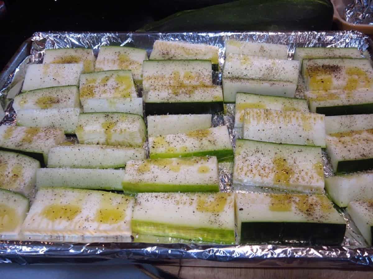 Olive oil drizzled zucchini on a baking sheet before roasting.