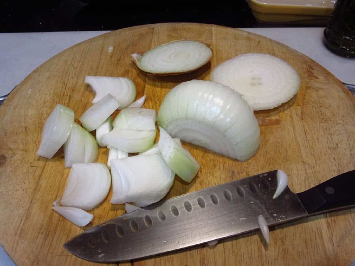 A sliced onion on a wooden cutting board with a knife.