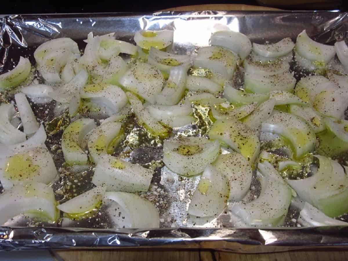 Onion slices with oil and pepper on a baking sheet before roasting.