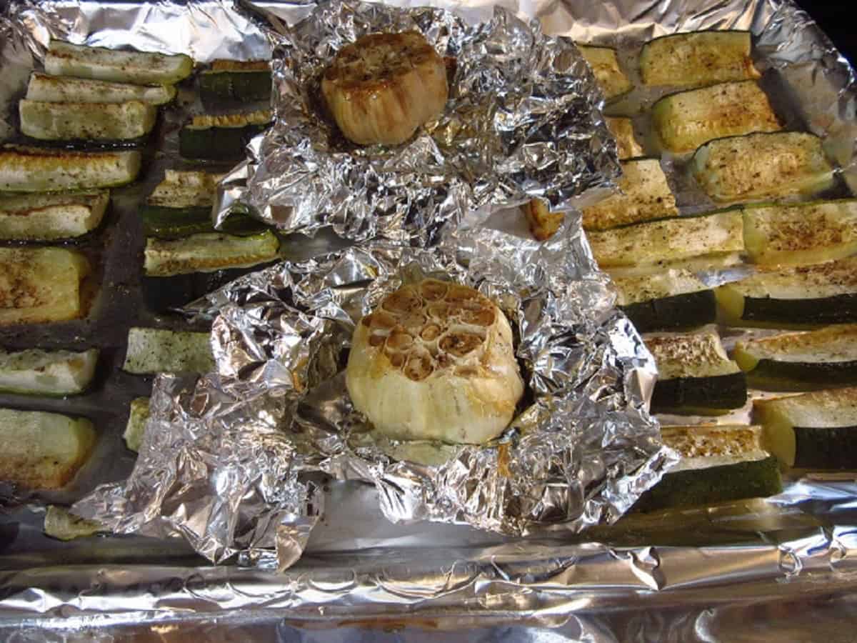 Roasted garlic bulbs and zucchini on a foil lined baking sheet.