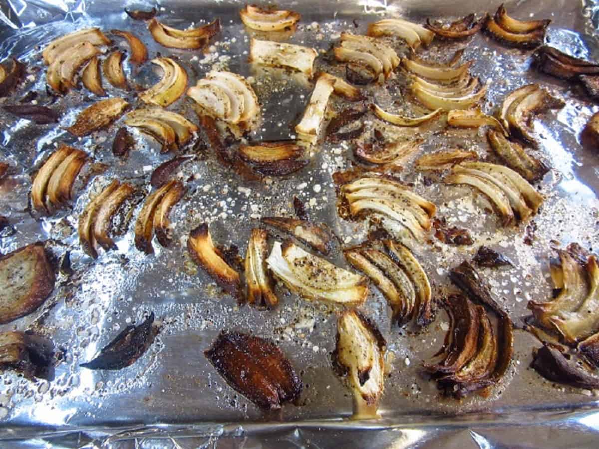 Deeply roasted onion slices on a foil lined baking sheet.