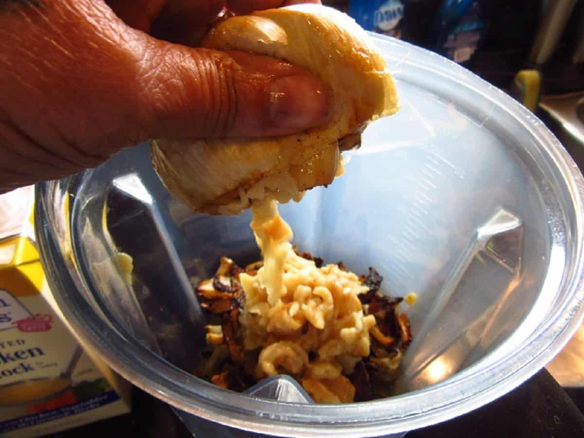 Roasted garlic being squeezed into a blender making soup.