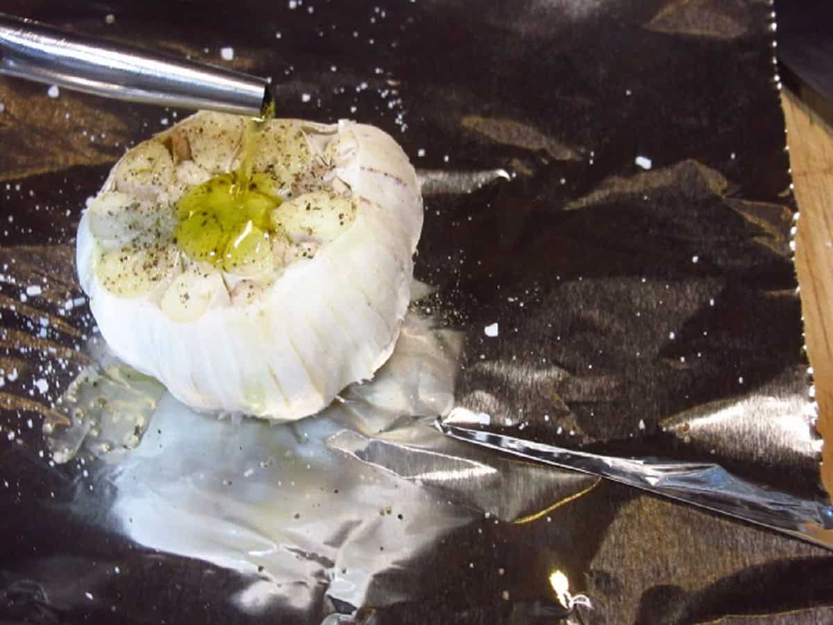 A bulb of garlic being drizzled with olive oil.