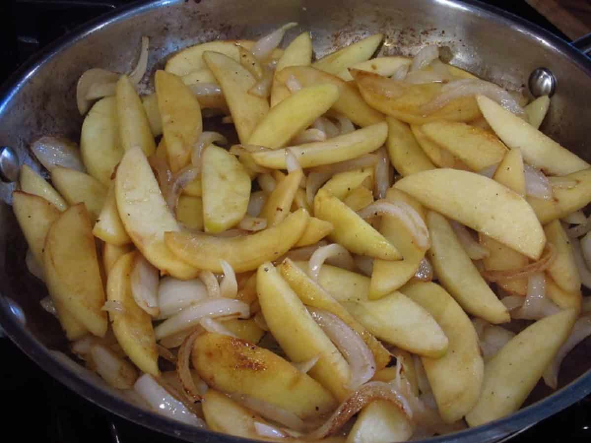 Cooking apple and onion slices in a large skillet.
