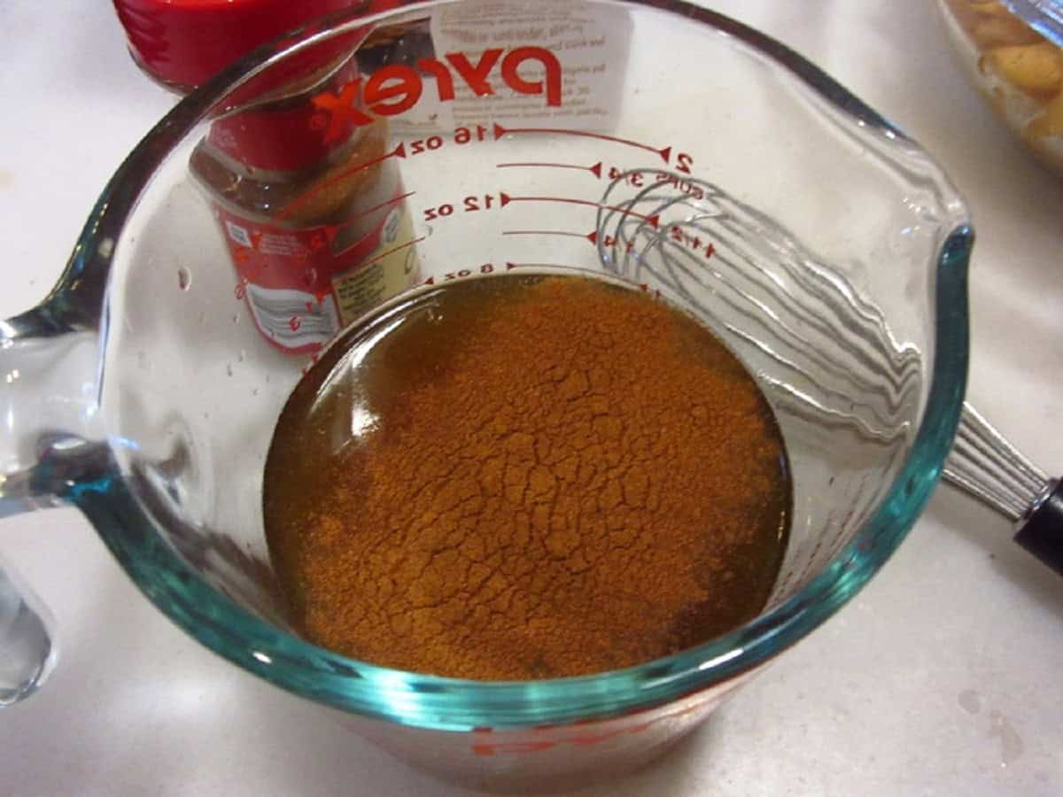 Chicken stock and ground cinnamon in a glass measuring cup.