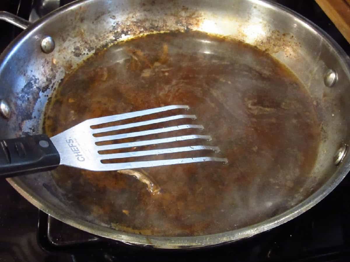A slotted spatula in a large silver skillet with liquid.