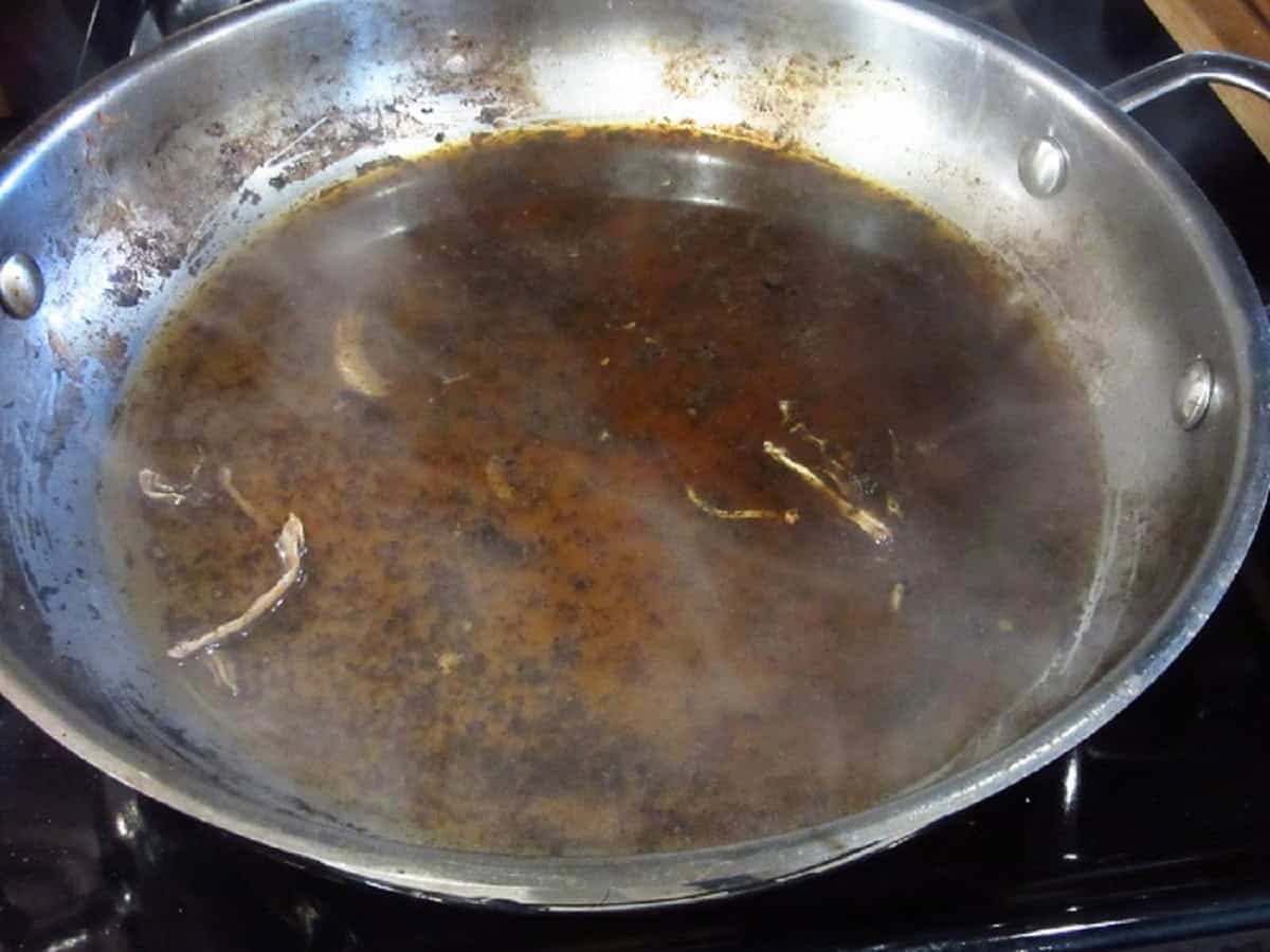 A silver skillet being deglazed with liquid.