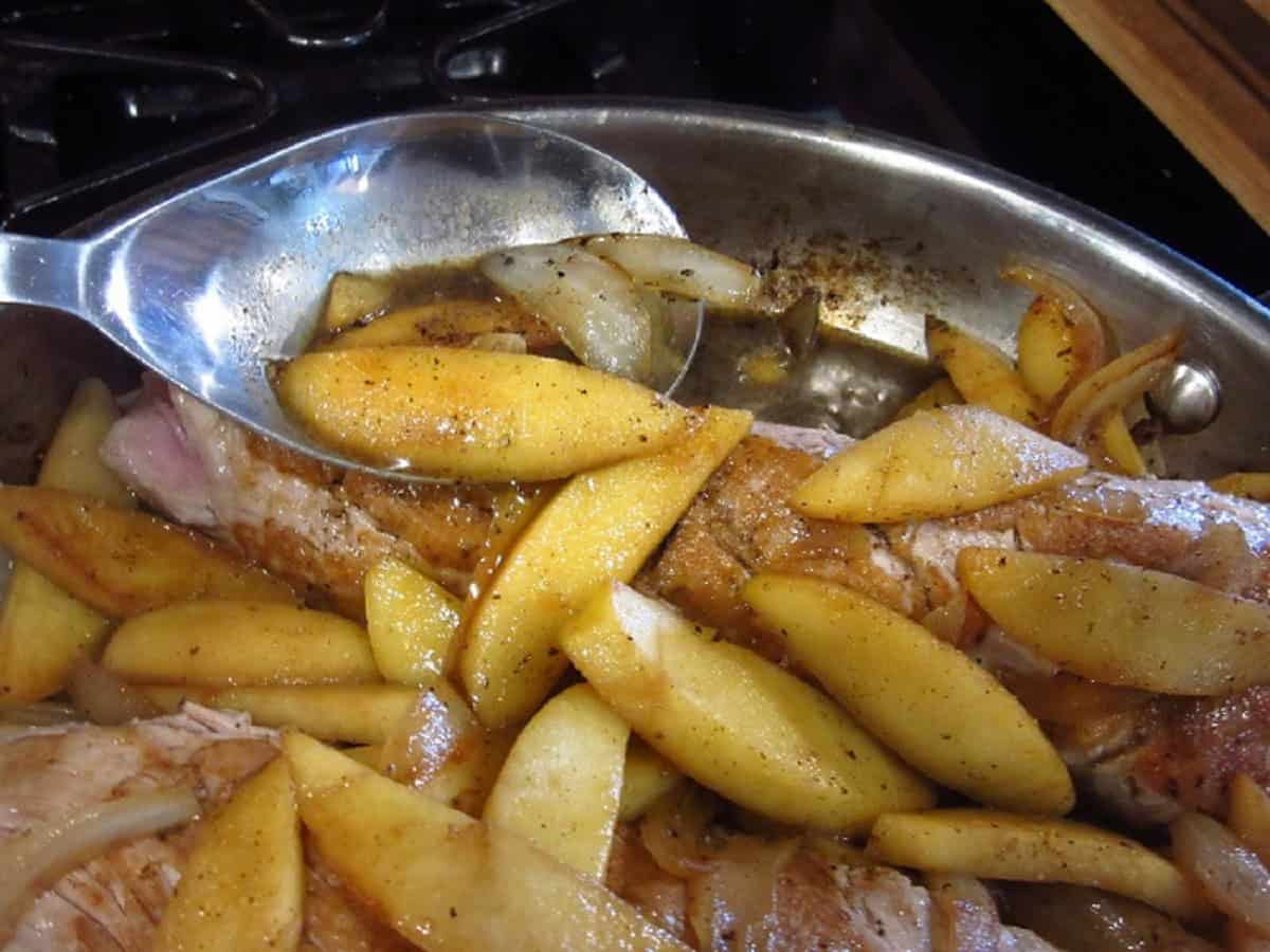 Cooked apples and onions in a large skillet with a big spoon.