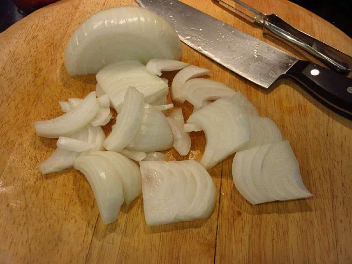 Sliced onions on a wooden cutting board.
