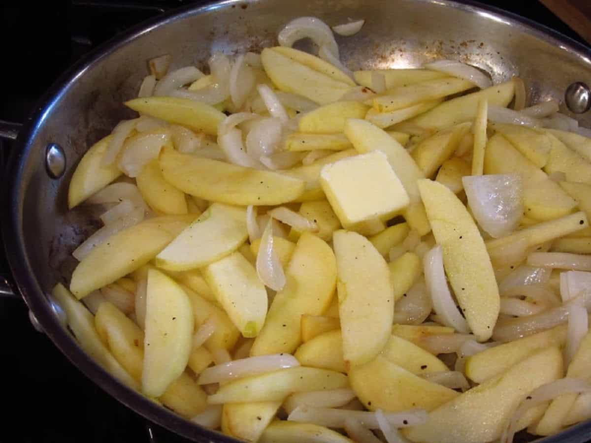 A pat of butter in a large skillet with apple and onion slices.