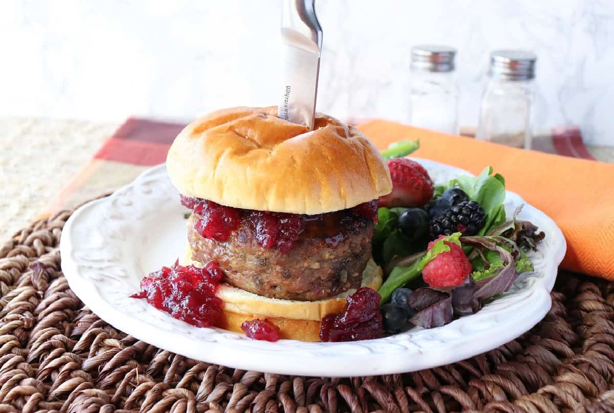 A turkey burger topped with cranberry sauce and a bon on a plate.