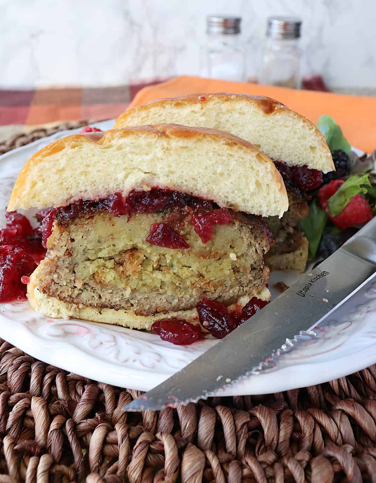 A cut in half stuffing stuffed turkey burger on a white plate with cranberry sauce.
