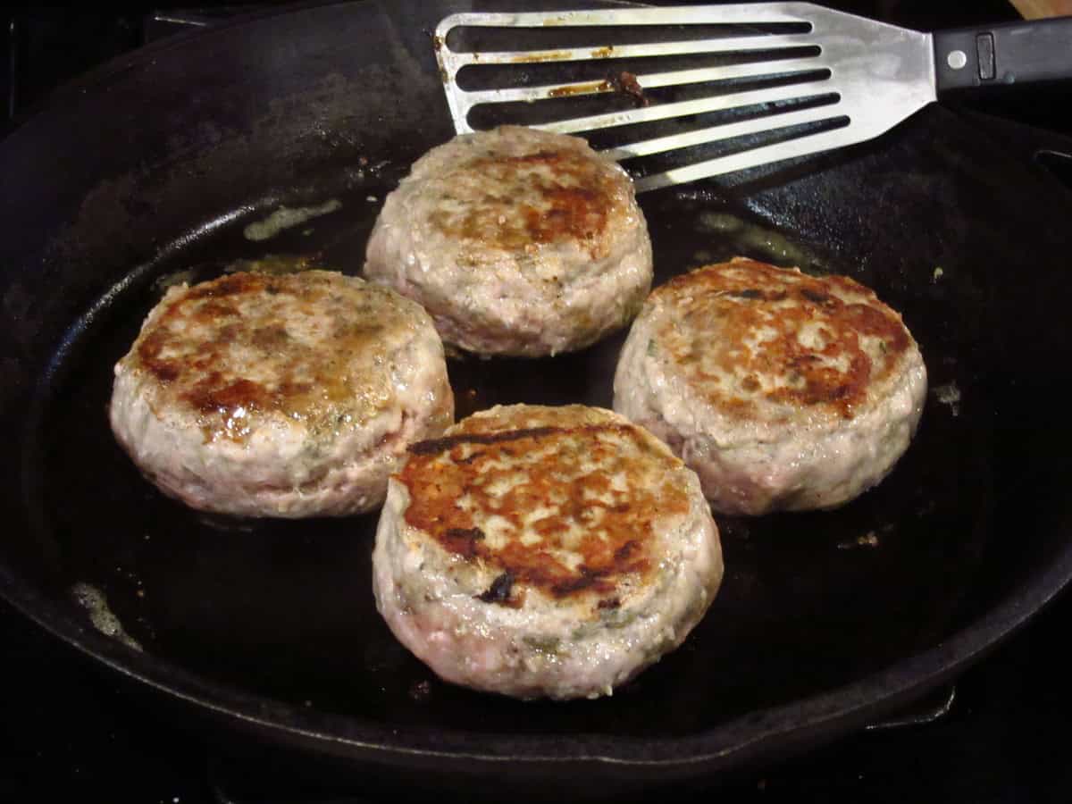 Four browning turkey burgers in a cast iron skillet.