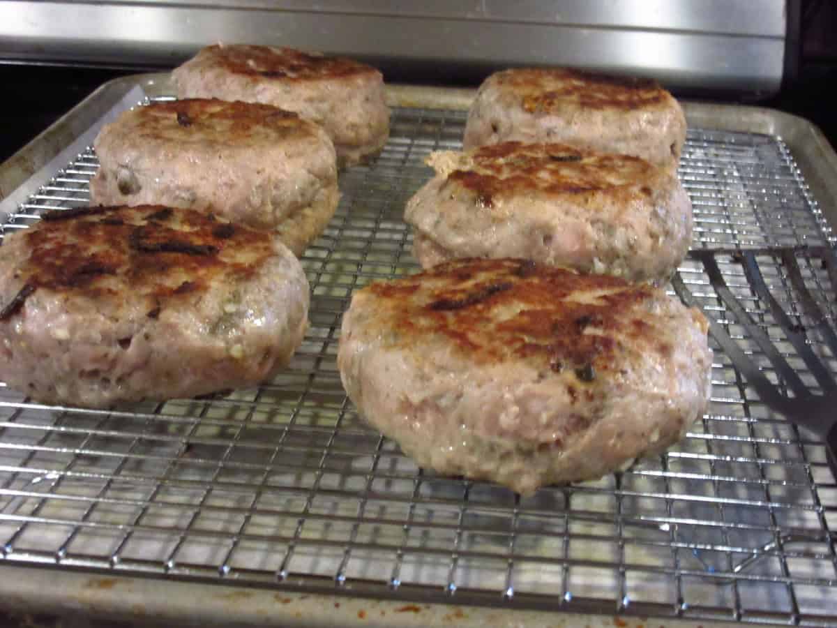 Six partially cooked turkey burgers on a rack before going into the oven.
