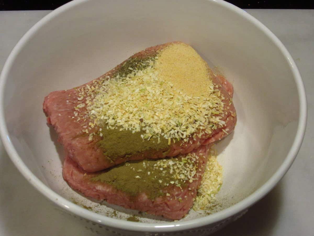Two pounds of ground turkey in a white bowl with spices and seasonings.
