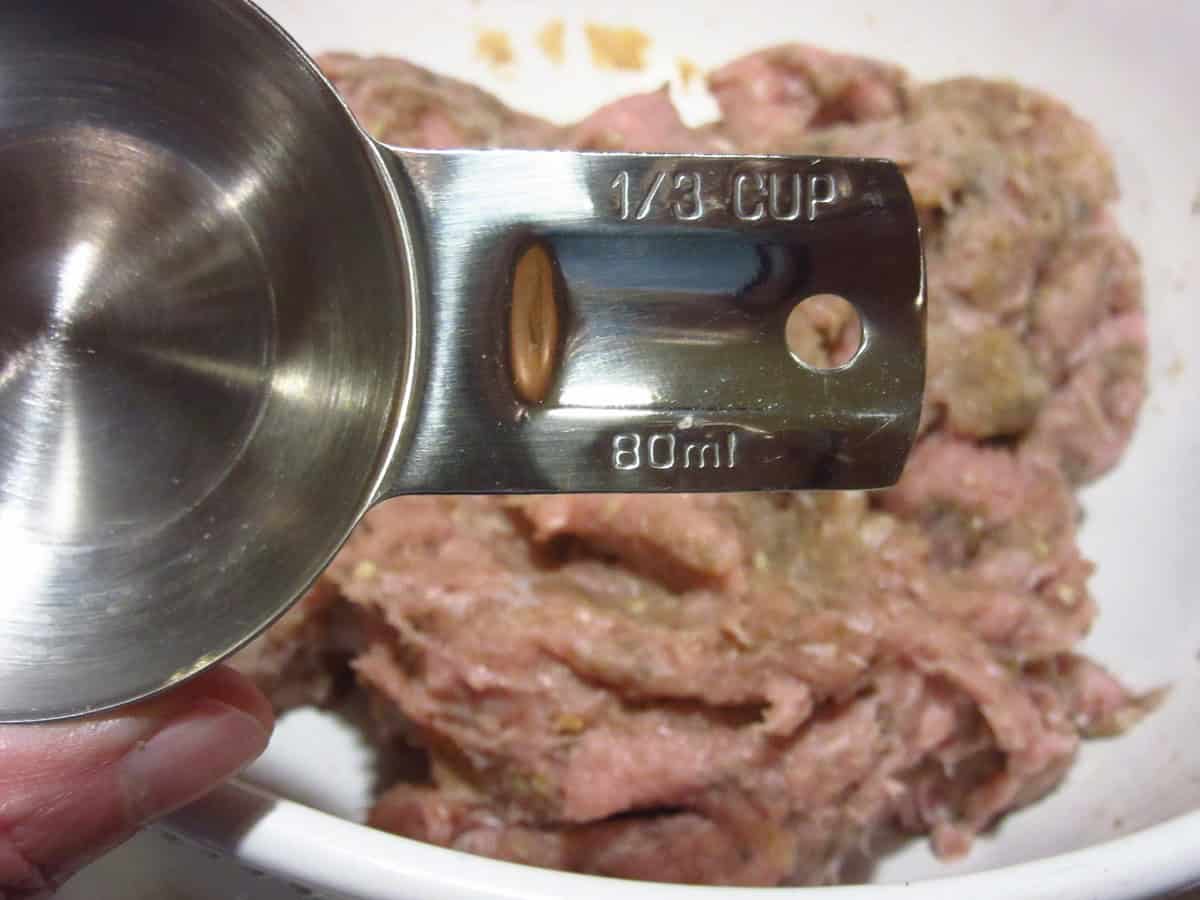 One third cup measuring cup being held over a bowl of ground turkey.