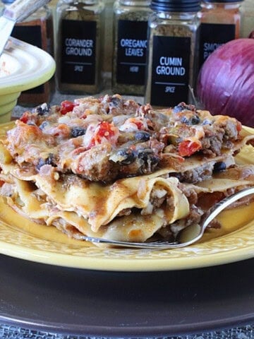 A hearty slice of Mexican Turkey Taco Lasagna on a yellow plate with a fork.