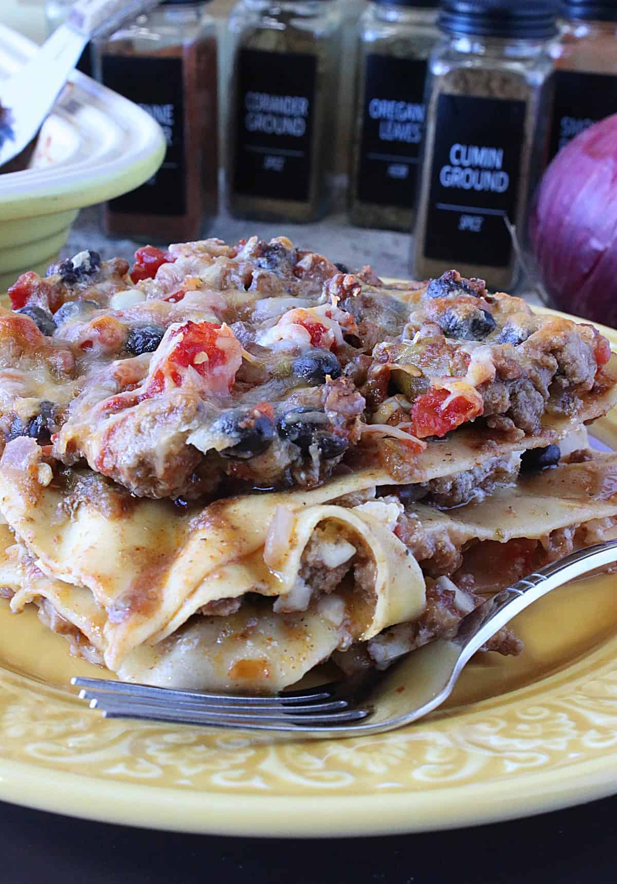 A fork on a plate with a serving of Turkey Taco Lasagna with black beans and cheese.