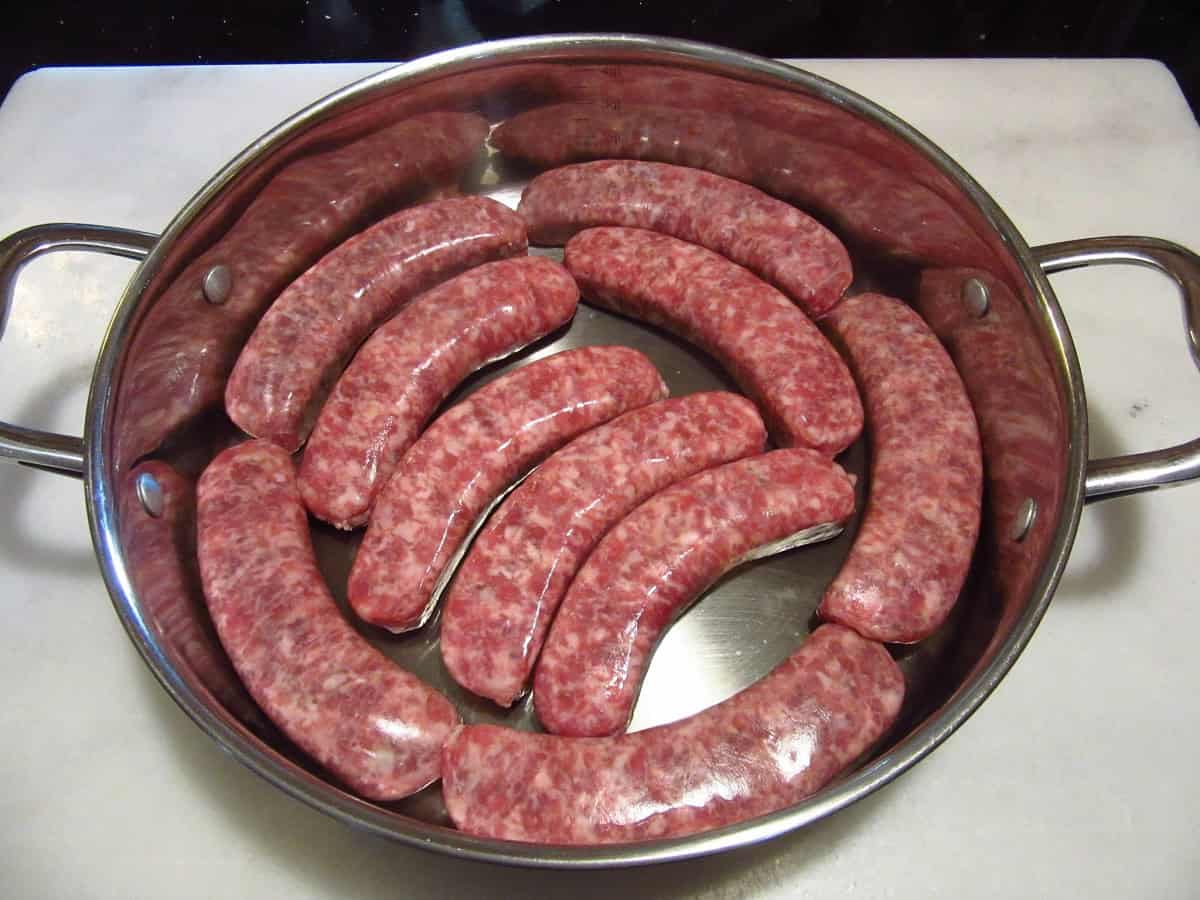 Uncooked bratwurst in a skillet.