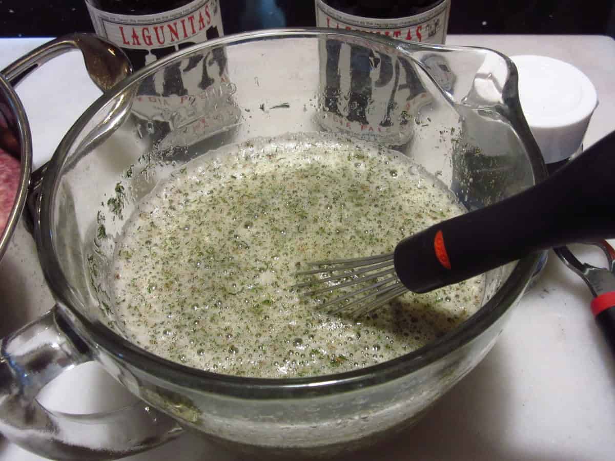 A glass measuring cup with beer and a whisk inside.