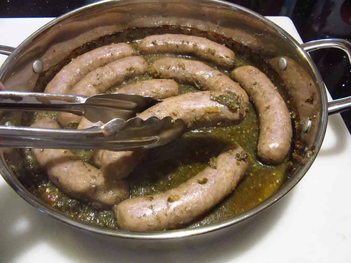 Tongs holding a bratwurst from a skillet.