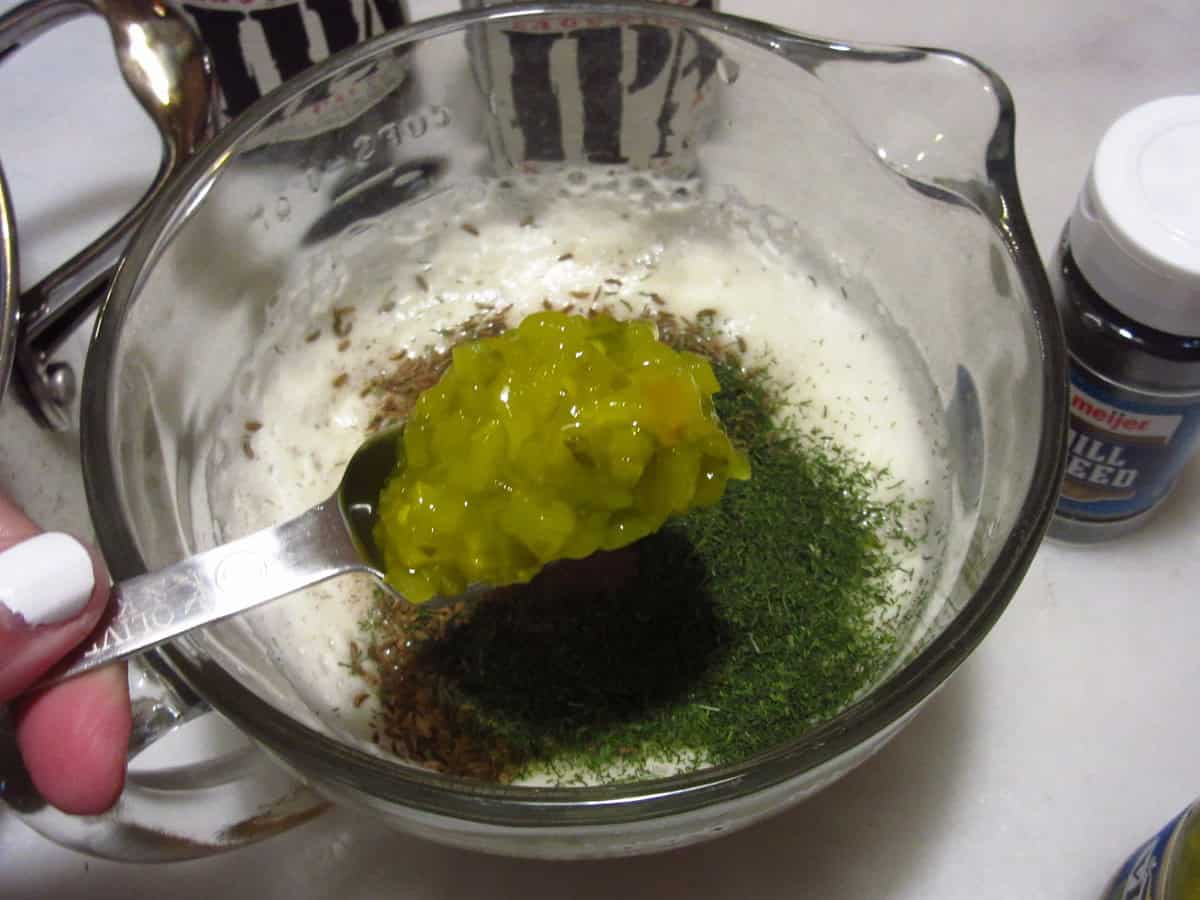 A spoonful of relish being added to a glass measuring cup.