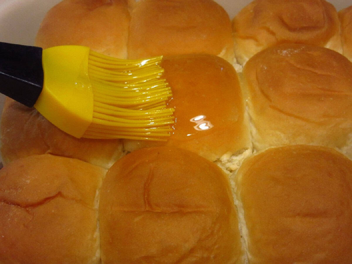 Melted butter being brushed on top of buns to make big mac sliders.
