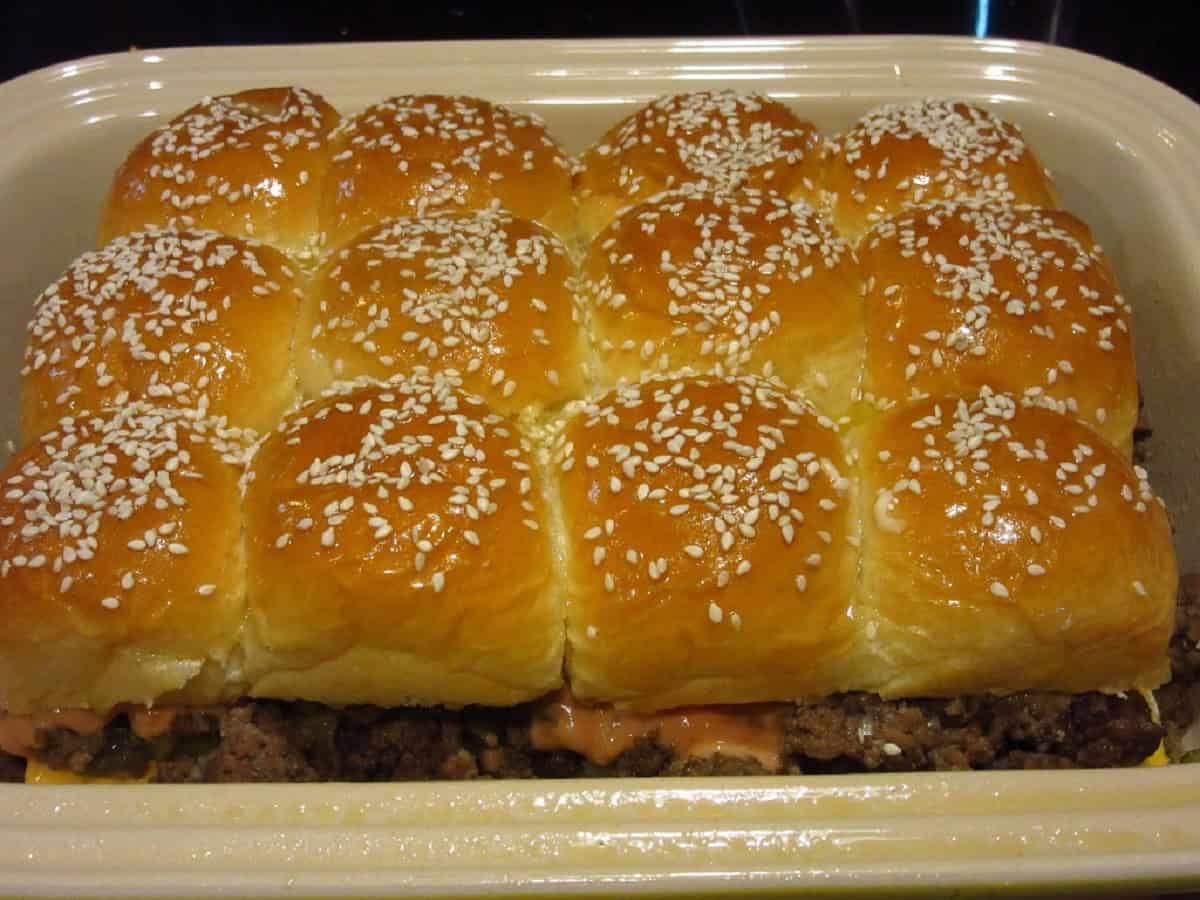 Sesame seed buns on top of big mac sliders in a casserole dish.
