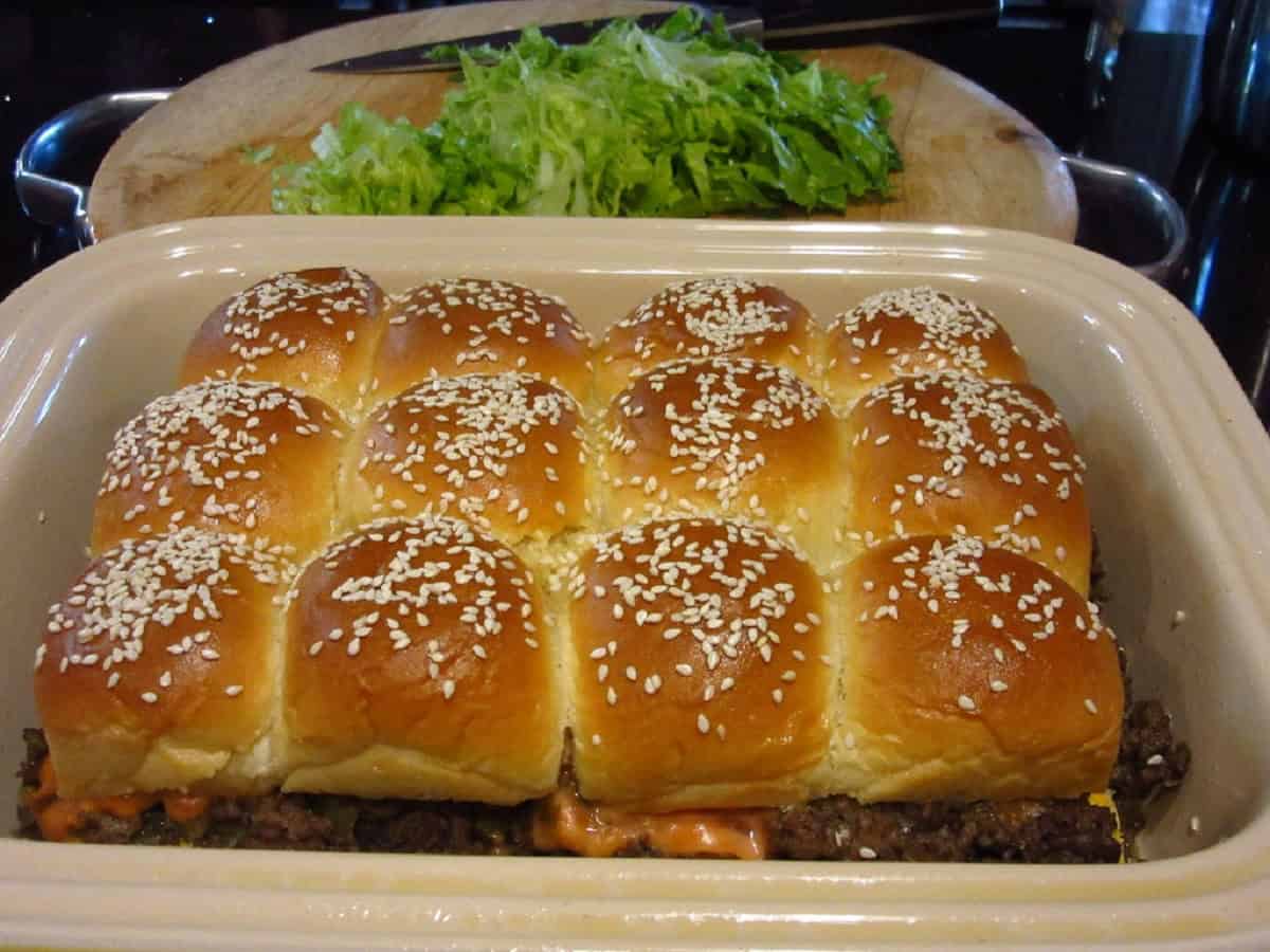 Shredded lettuce in the background of a casserole dish filled with big mac sliders.