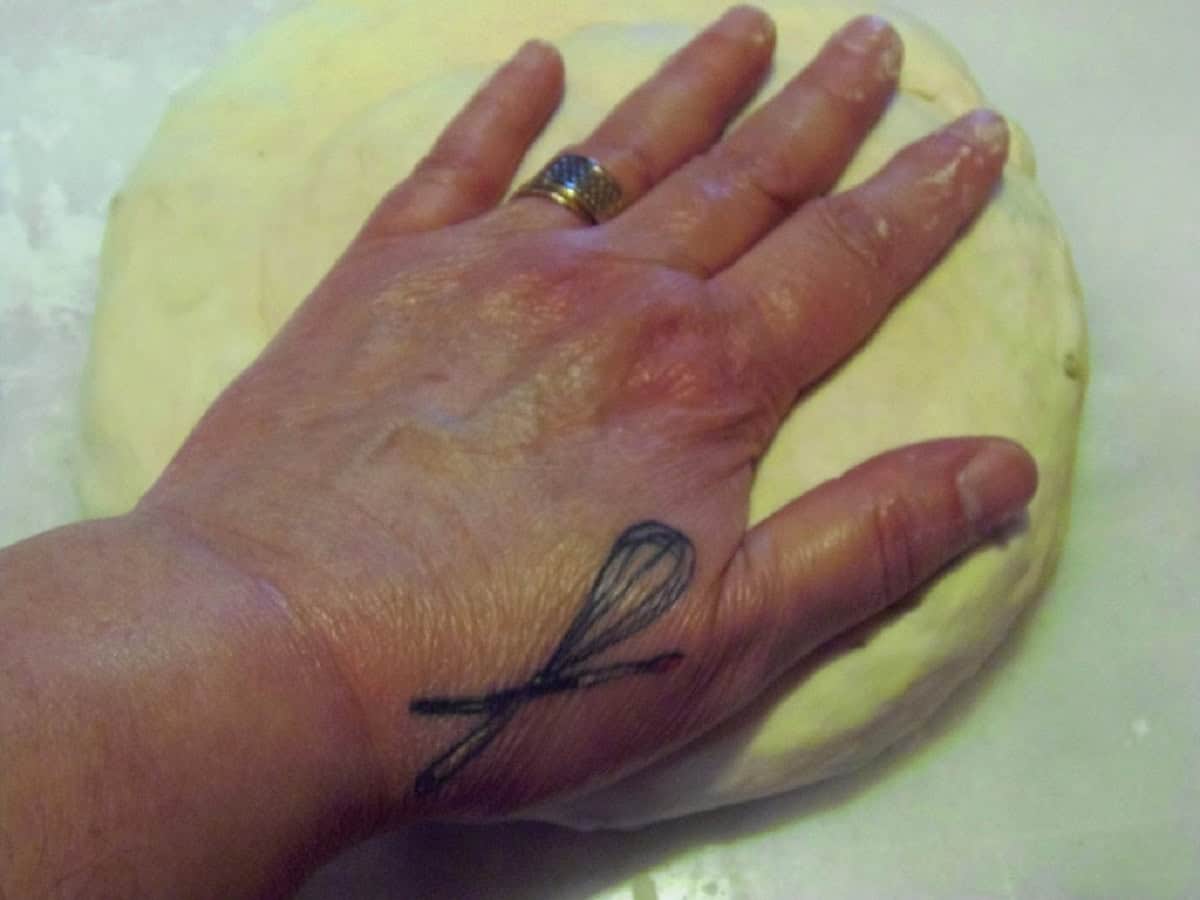 A hand pressing down a circle of bread dough.