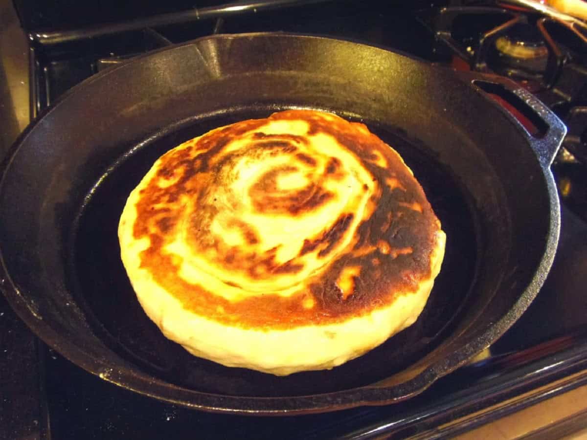 A golden round loaf of Chinese Bing Bread in a cast iron skillet.