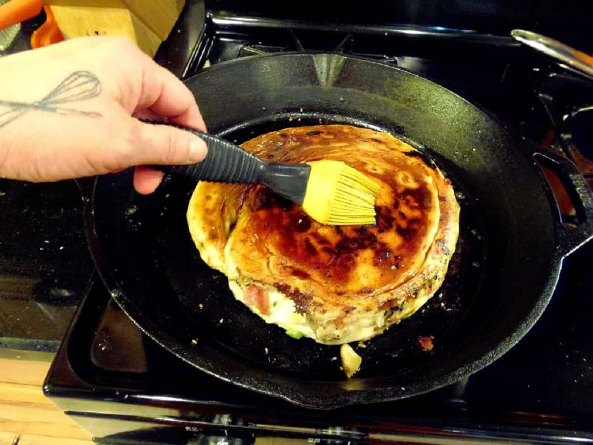 A hand brushing sesame seed oil on a cooking loaf of Chinese Bing Bread.