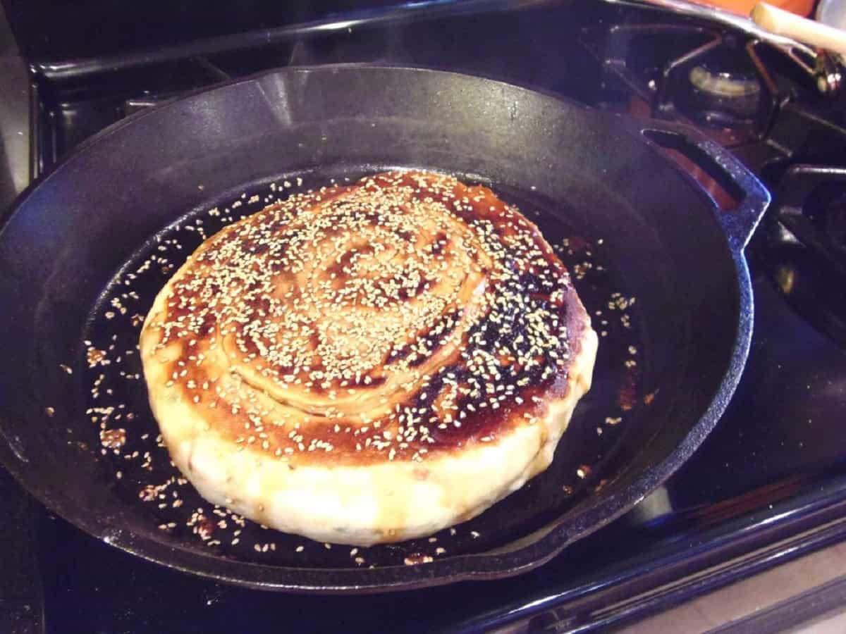 A coiled, round loaf of Chinese Bing bread cooking in a cast iron skillet.