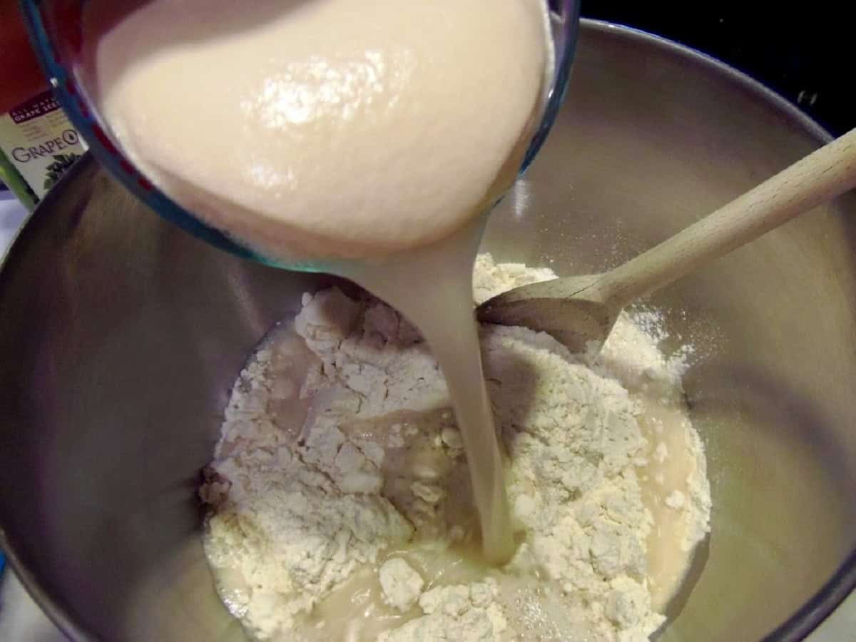 Foamy yeast being poured into a bowl of flour.