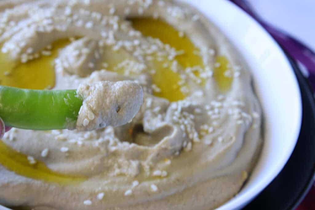 A closeup of a sugar snap pea after being dipped into Roasted Eggplant and Chickpea Hummus.