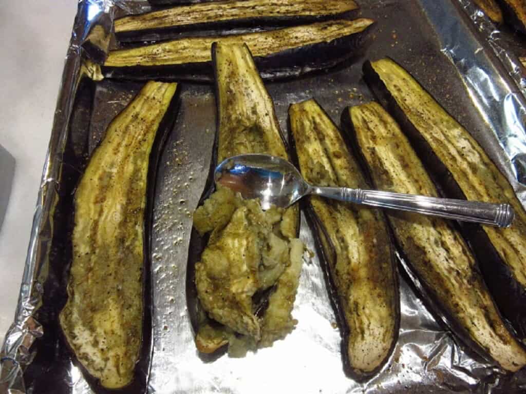 A spoon scooping out the flesh from the inside of roasted eggplants.
