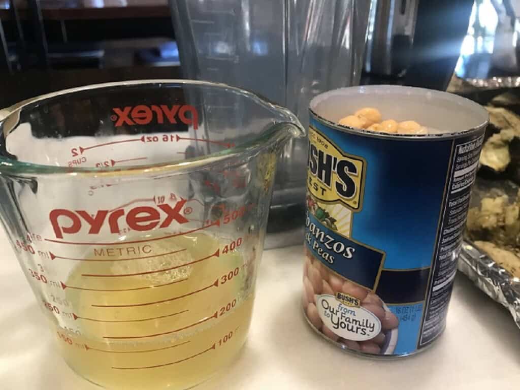 A drained can of chickpeas with their liquid in a glass measuring cup.