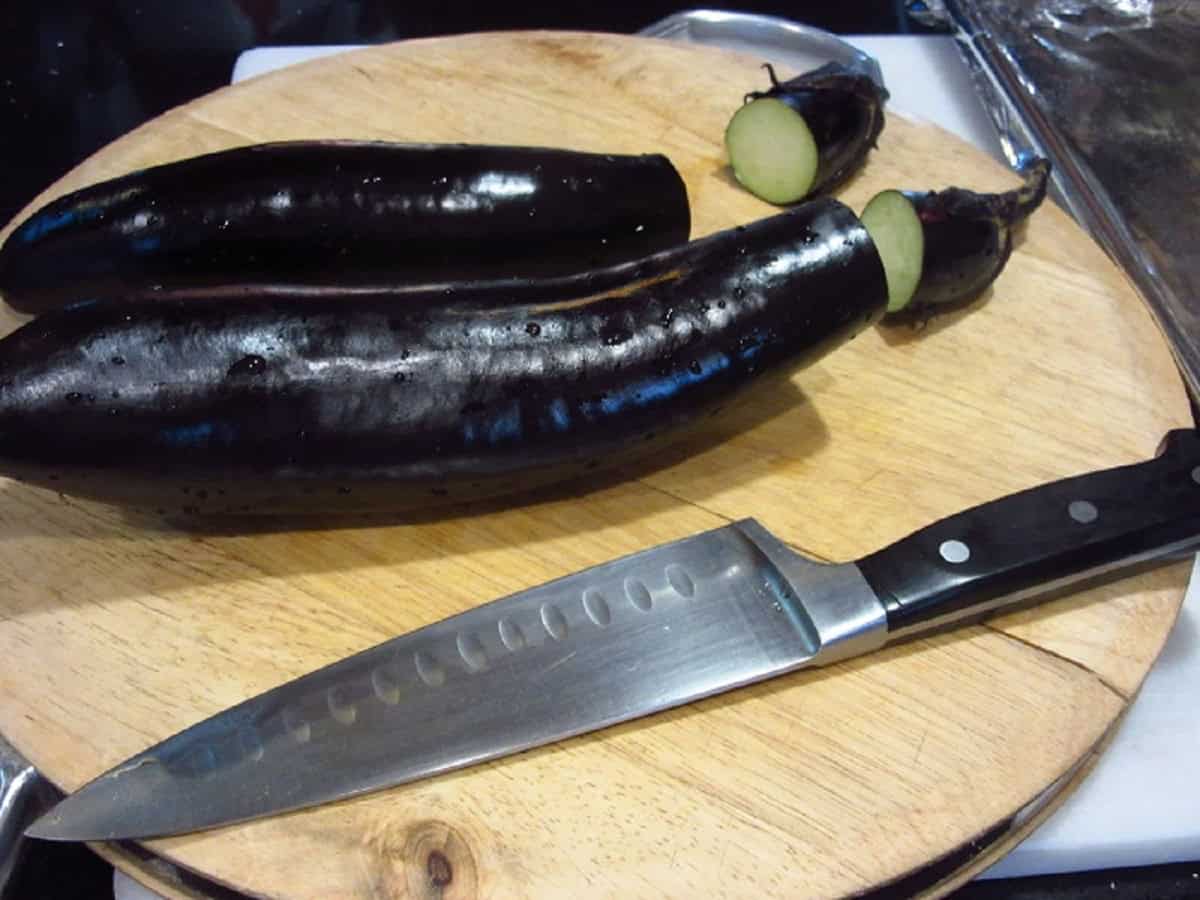 Two long eggplants on a cutting board with a knife.