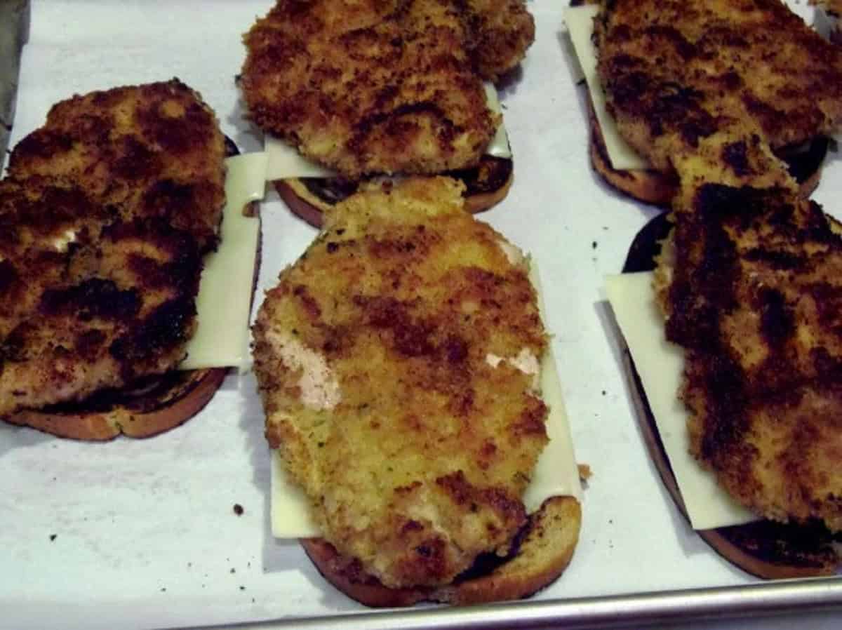 Breaded pork cutlets on marbled rye bread and on top of Swiss cheese slices.