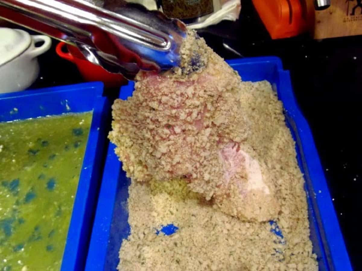 A pair of tongs holding up a breaded pork schnitzel.