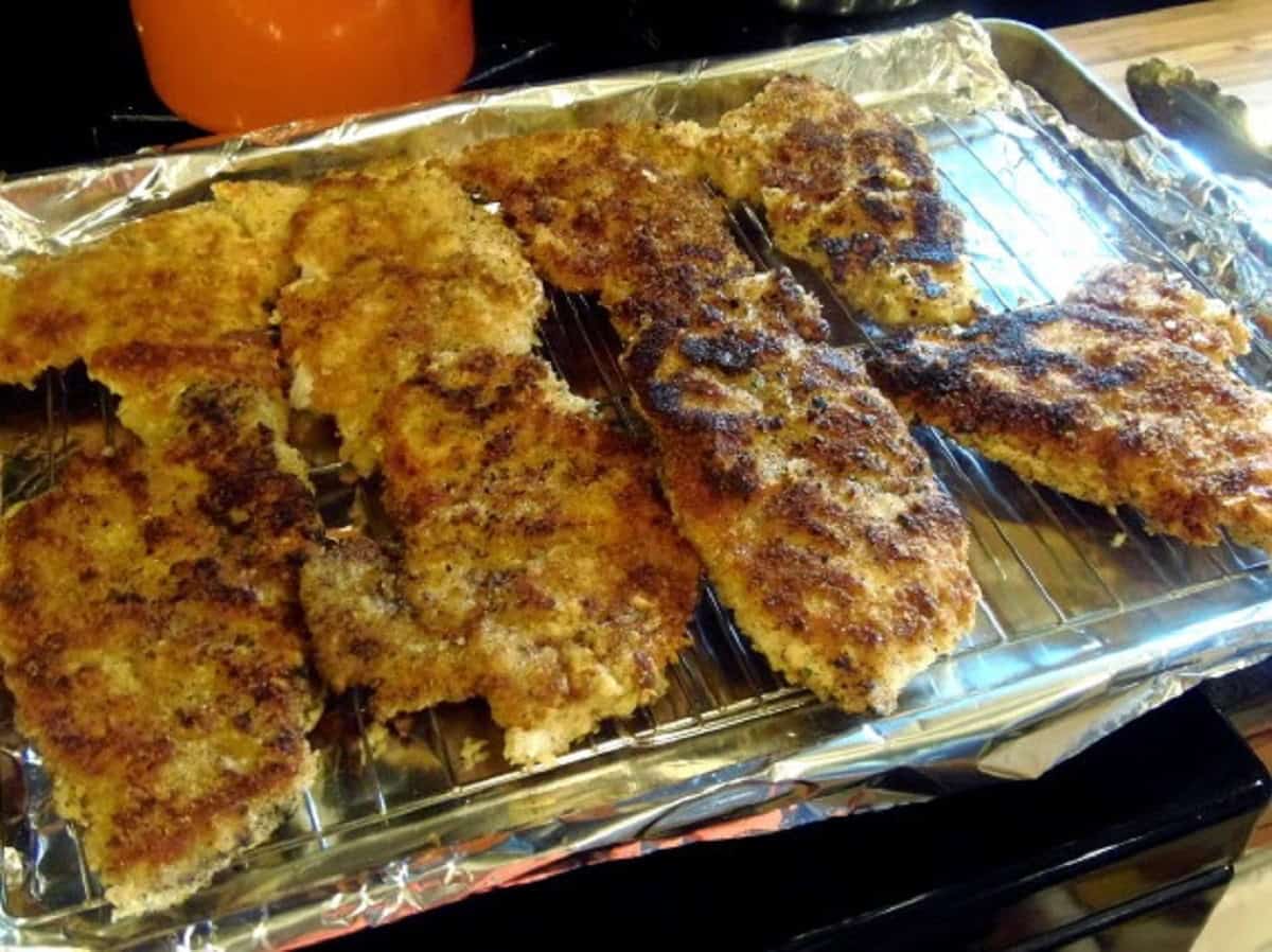 A bunch of breaded pork cutlets on a baking sheet.