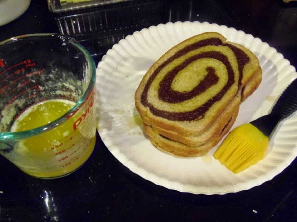 Slices of marbled rye bread on a paper plate with melted butter on the side.