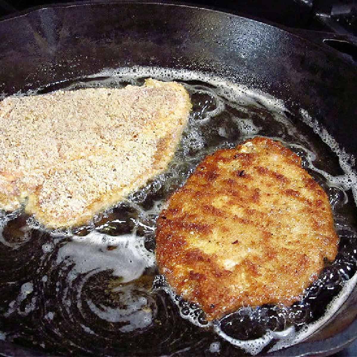 Two breaded pork cutlets in a frying pan.