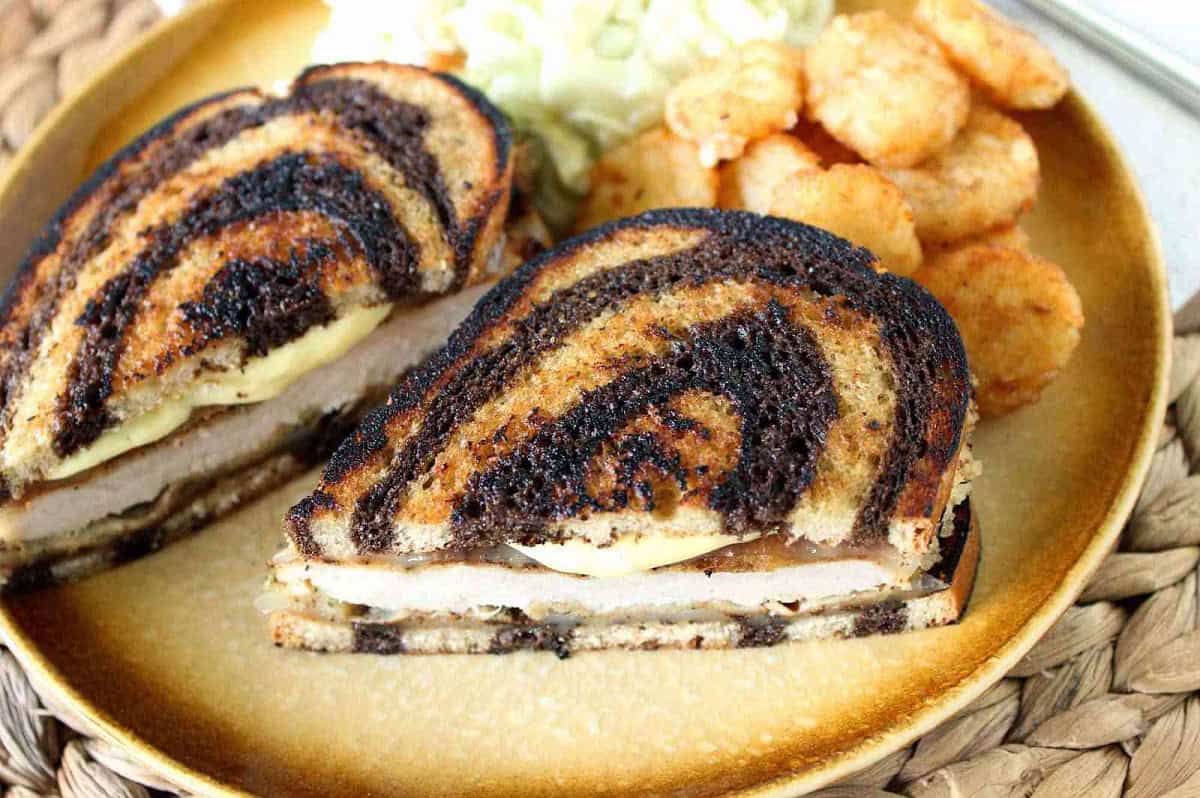 A marbled rye bread Pork Schnitzel Melt Sandwich on a golden colored plate.