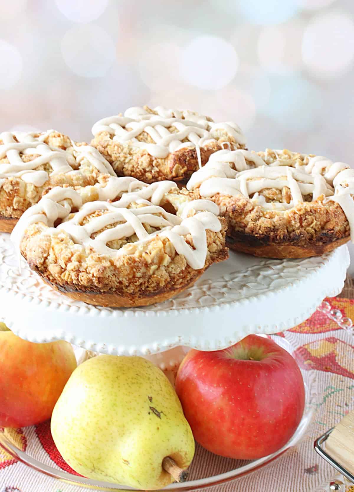 A cake stand with four apple and pear blossoms on top and real apples and pears underneath.