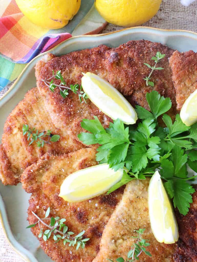 Golden brown Pork Schnitzel with lemon and thyme on a platter.