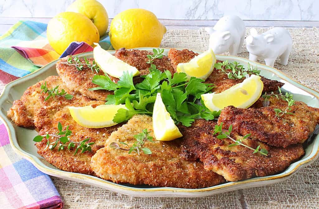 A platter filled with golden brown Pork Schnitzel with lemon wedges and fresh herbs.