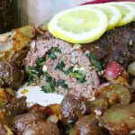 A delicious Rolled Greek Meatloaf slice topped with lemons and surrounded by potatoes.
