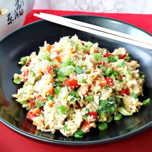 A black bowl filled with colorful Brown Rice Stir Fry and some chip sticks.